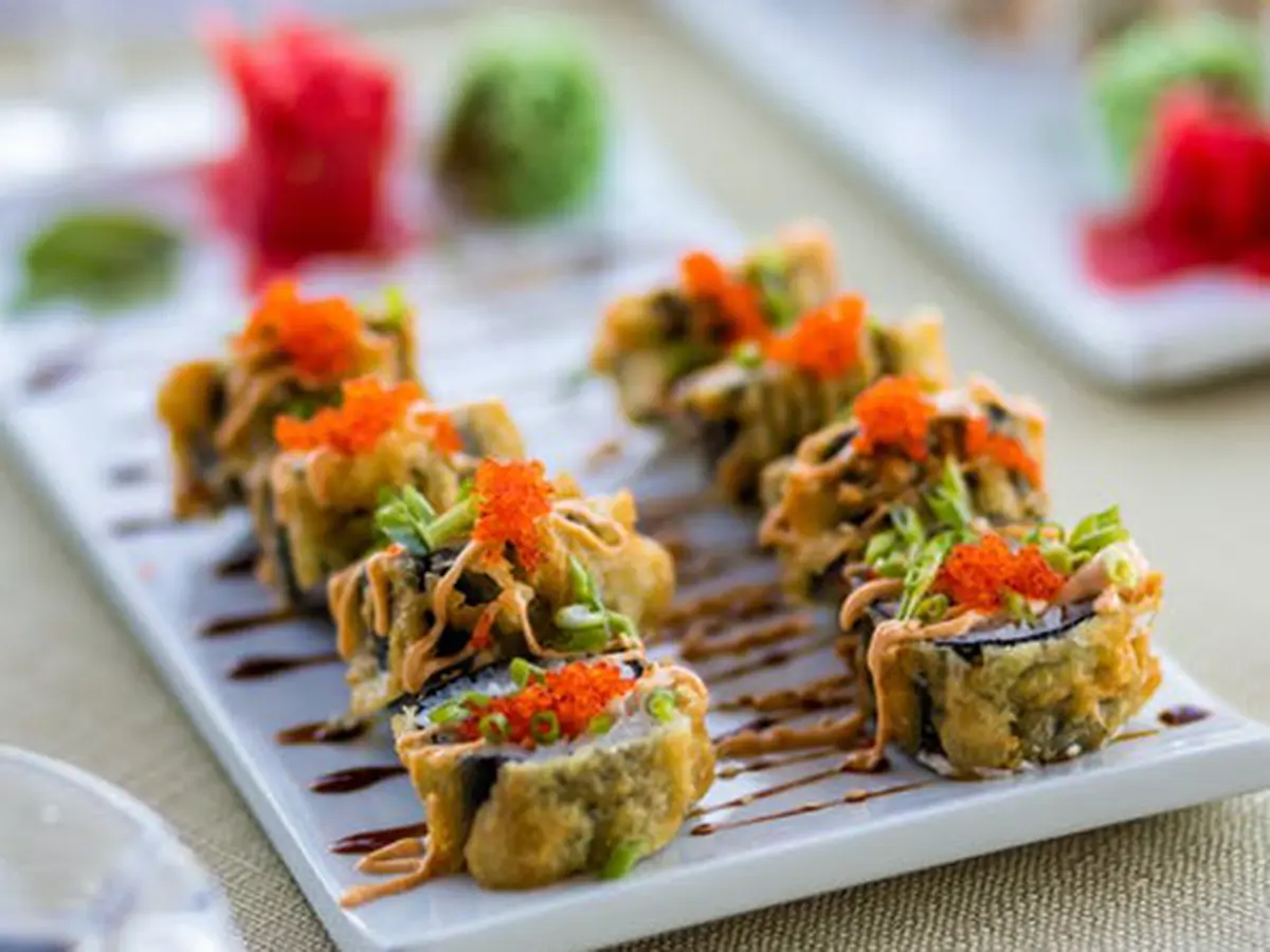 Tempura sushi rolls topped with orange fish roe and creamy sauce on white plate at Cucumber Sushi, a Japanese Restaurant in Jersey City