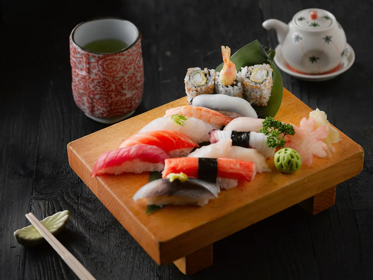 Wooden sushi board with assorted nigiri, maki, green tea and teapot set at Cucumber Sushi, a Japanese Restaurant in Jersey City