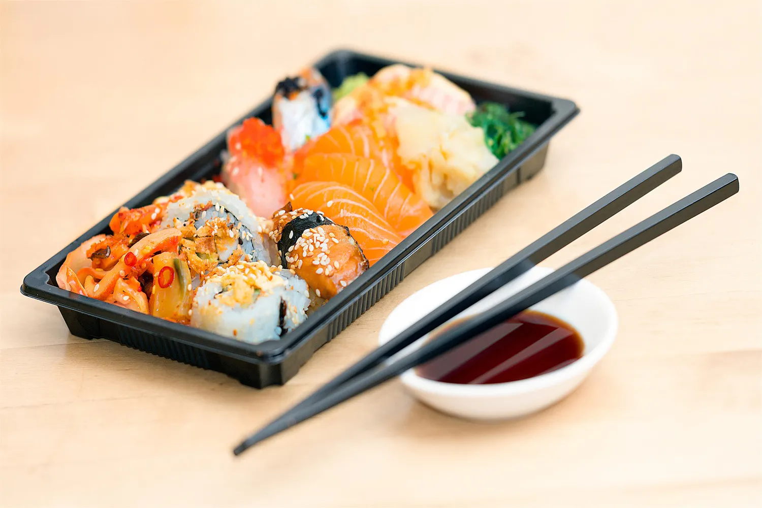 Takeout plastic sushi box with mixed sashimi, maki and side soy sauce dish at Cucumber Sushi, a Japanese Restaurant in Jersey City